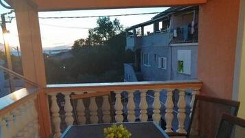 Un balcón con mesa y sillas, una planta en maceta y vista de edificios al fondo.