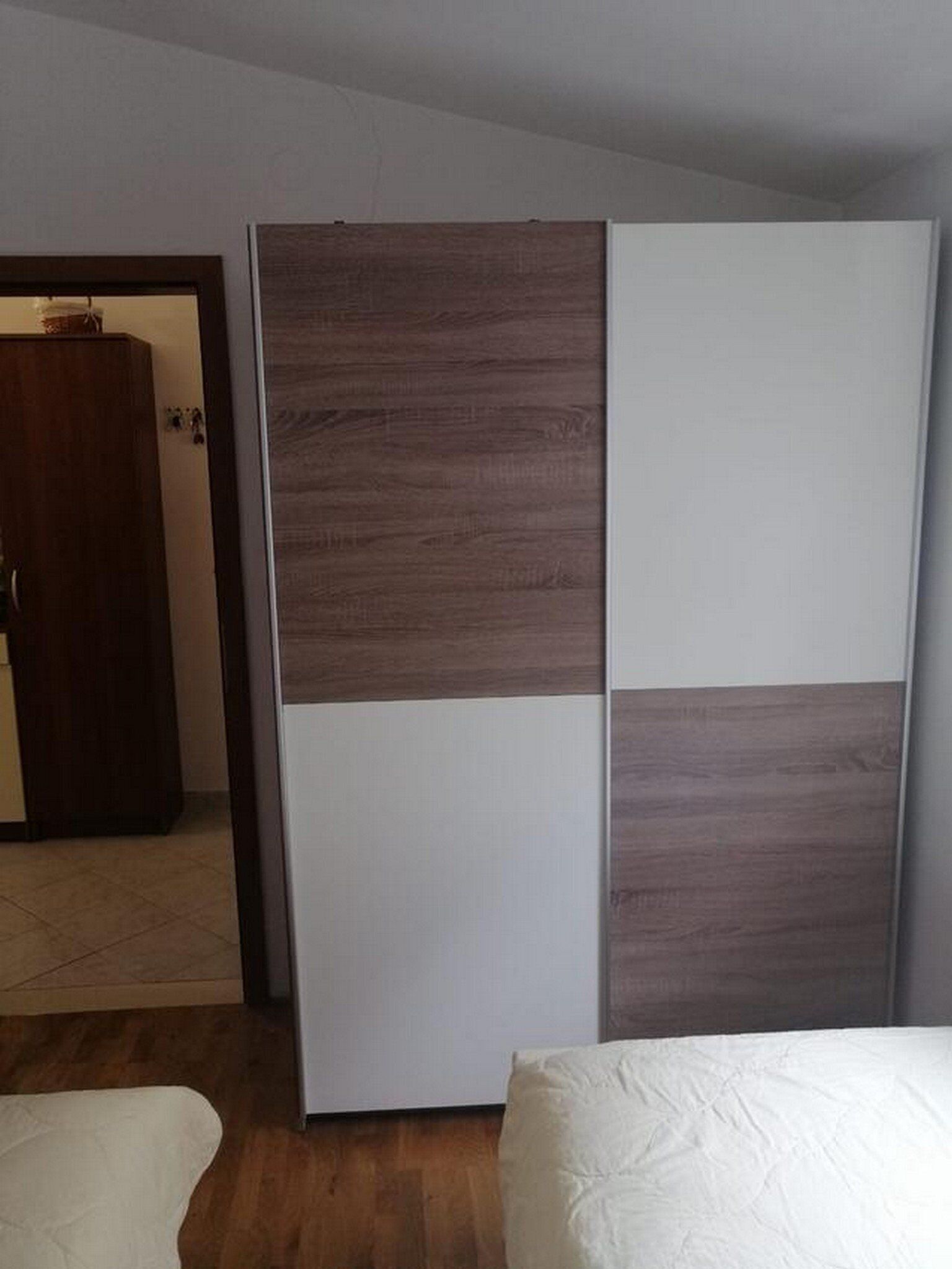 A bedroom with a bed, a wardrobe with a brown and white panel design, and a wooden floor.