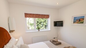 A bedroom with a bed, a window with a view of trees, a radiator, a television, and a framed picture on the wall. - Foulsyke Farm Bungalow (Saltburn-by-the-Sea)