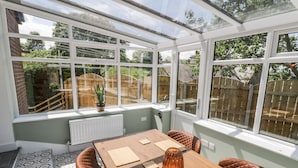 A conservatory with a wooden table and chairs, a potted plant, and a view of a garden. - Foulsyke Farm Bungalow (Saltburn-by-the-Sea)