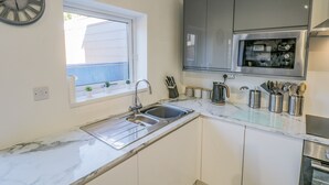A kitchen with a sink, a window, cabinets, a clock, and a microwave. - Cliff House (Saltburn-by-the-Sea)