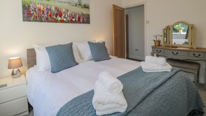 A neatly made bed with a blue quilt, white pillows, and two rolled towels. A painting of a field of flowers hangs on the wall. - Cliff House (Saltburn-by-the-Sea)