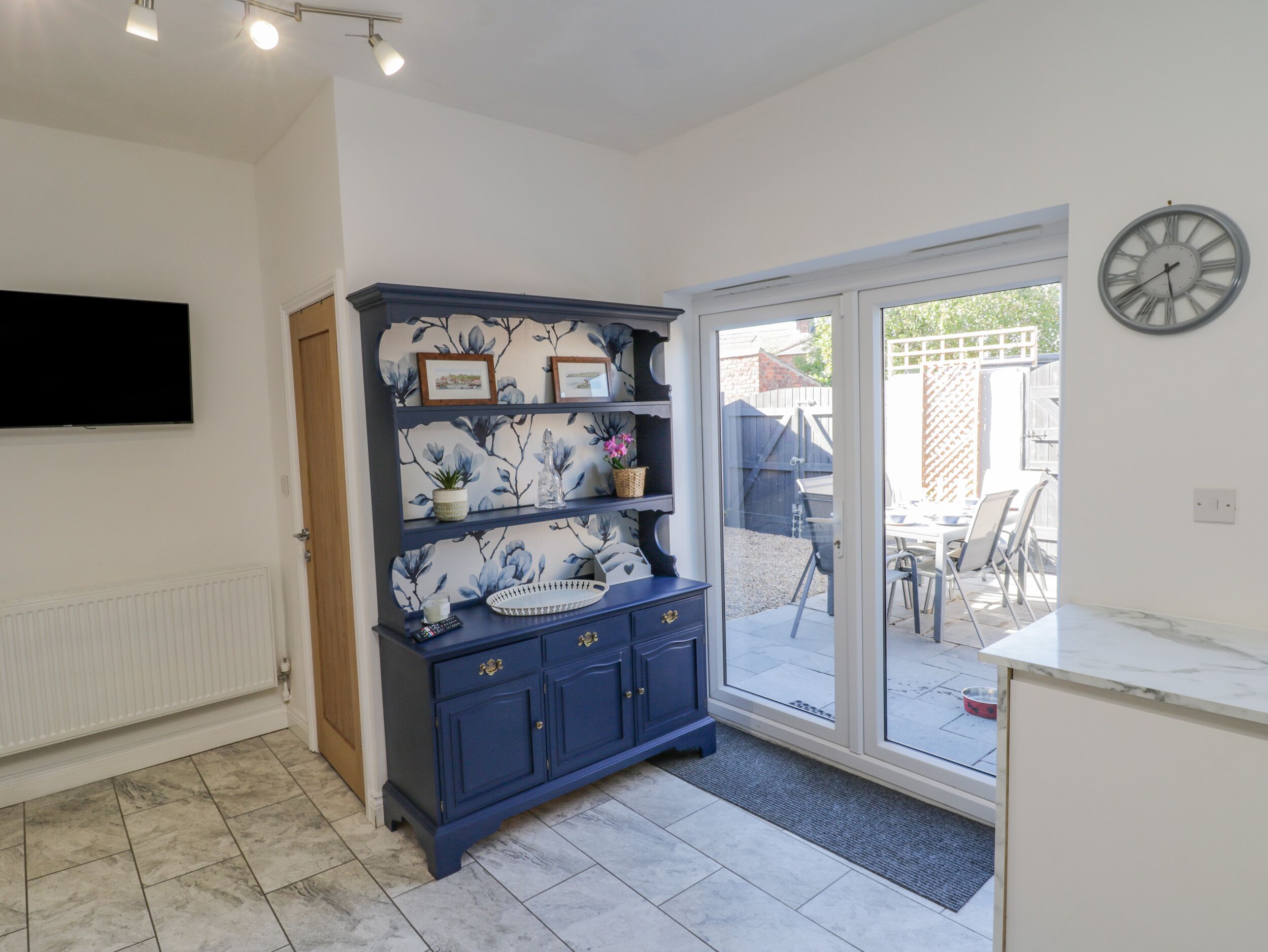 A kitchen with a blue cabinet, a wall-mounted TV, and a sliding glass door leading to an outdoor patio.
