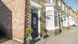 A two-story brick house with a black front door, white window frames, and a small garden with potted plants. - Cliff House (Saltburn-by-the-Sea)