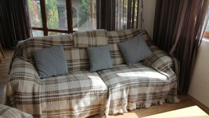 Un sofá estampado con diseño escocés y cojines en una habitación con ventanas amplias y cortinas.