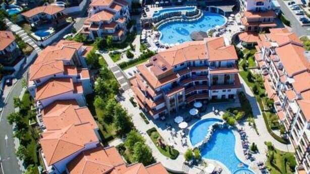 Un resort con varias edificaciones, un área de piscina central y vegetación circundante.