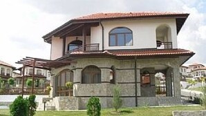 Una casa de dos pisos con fachada de piedra, un balcón en el piso superior y un porche cubierto.