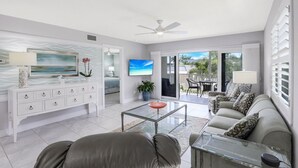 Un salon moderne avec une table basse en verre, un canapé, un téléviseur et un balcon aménagé avec du mobilier d’extérieur.