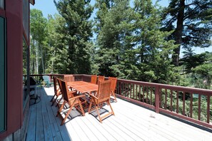Une terrasse en bois avec une table et des chaises, entourée de grands arbres.