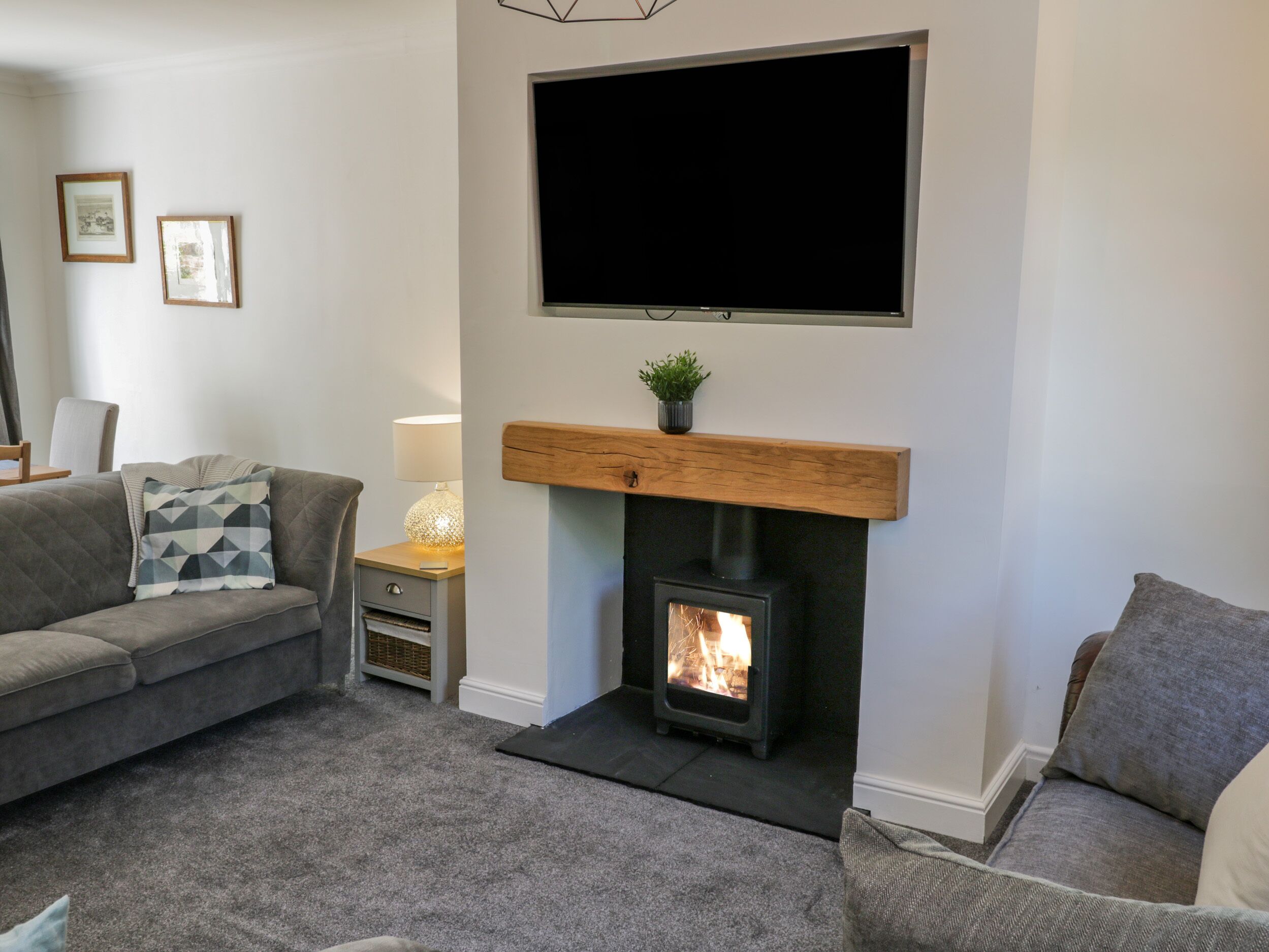 A living room with a fireplace, a sofa, a TV mounted above the fireplace, and a small table with a lamp.
