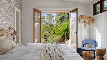 A bedroom with a bed, a chair, a bedside table, and a view of a garden through an open door.