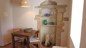 Een knus vertrek met een stenen plank waarop een theepot, bekers en een vaas staan. Er is een houten tafel met stoelen en een rieten mandje.