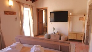 Een slaapkamer met een bed, een aan de muur bevestigde televisie, een houten garderobe en een spiegel.