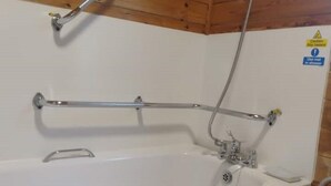 A white bathtub with chrome fixtures, a wooden ceiling, and a caution sign on the wall. - Beacon Lodge, accessible, family and dog friendly. (NEWQUAY)