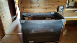 Un petit berceau portatif à roulettes, portant l’inscription « Jote », dans une pièce aux murs en bois et au sol recouvert d’une moquette.
