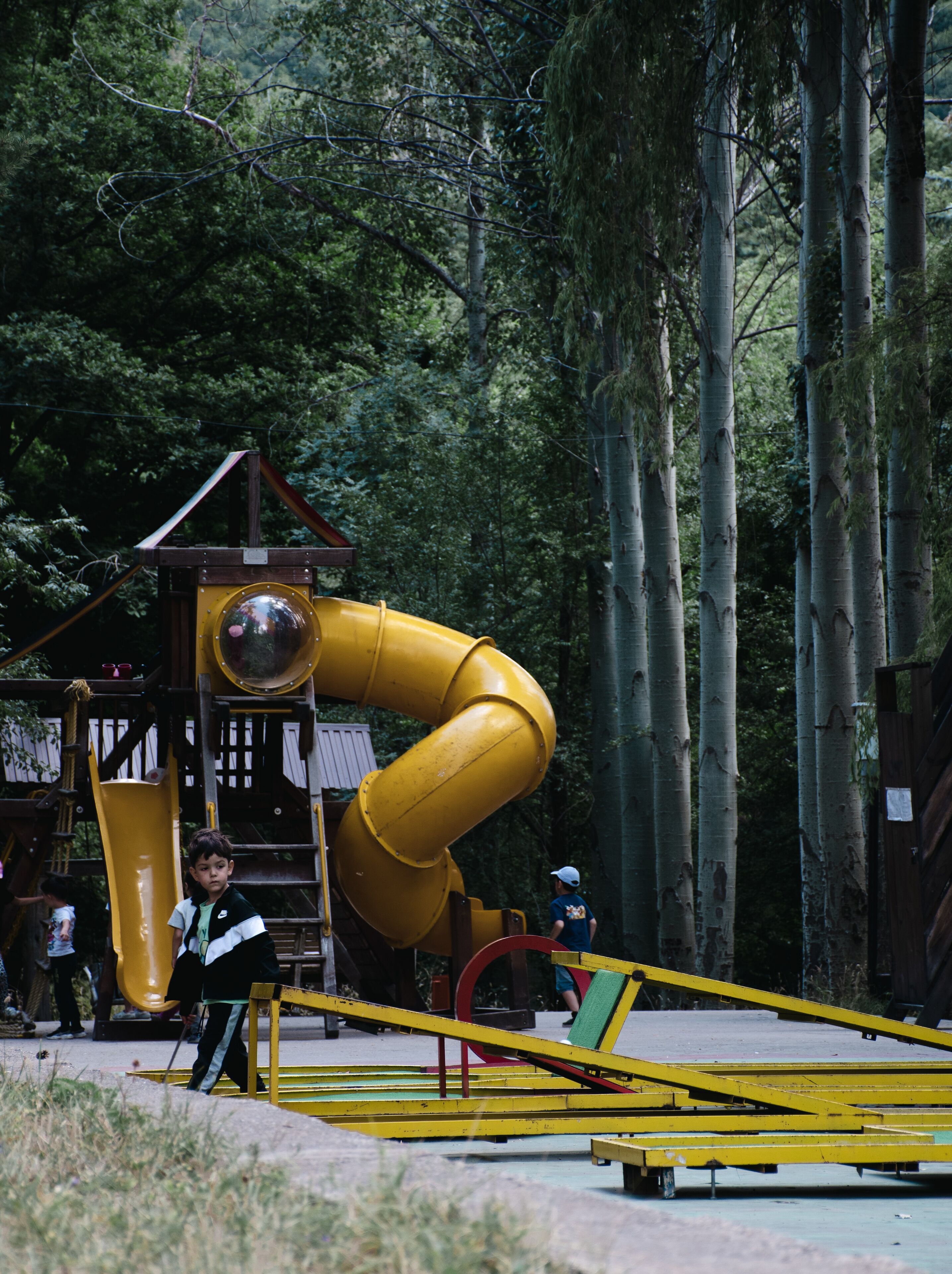 Un parc infantil amb un tobogan groc i una caseta de fusta.