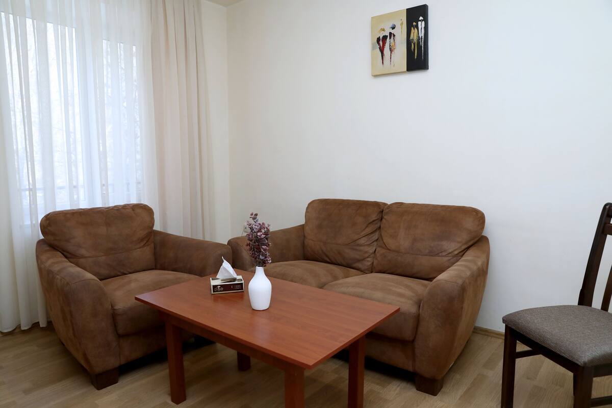 A living room with a brown sofa, a wooden coffee table, and a vase with flowers.