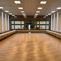 Una amplia sala de conferencias con una larga mesa, techos altos con iluminación lineal y grandes ventanales.