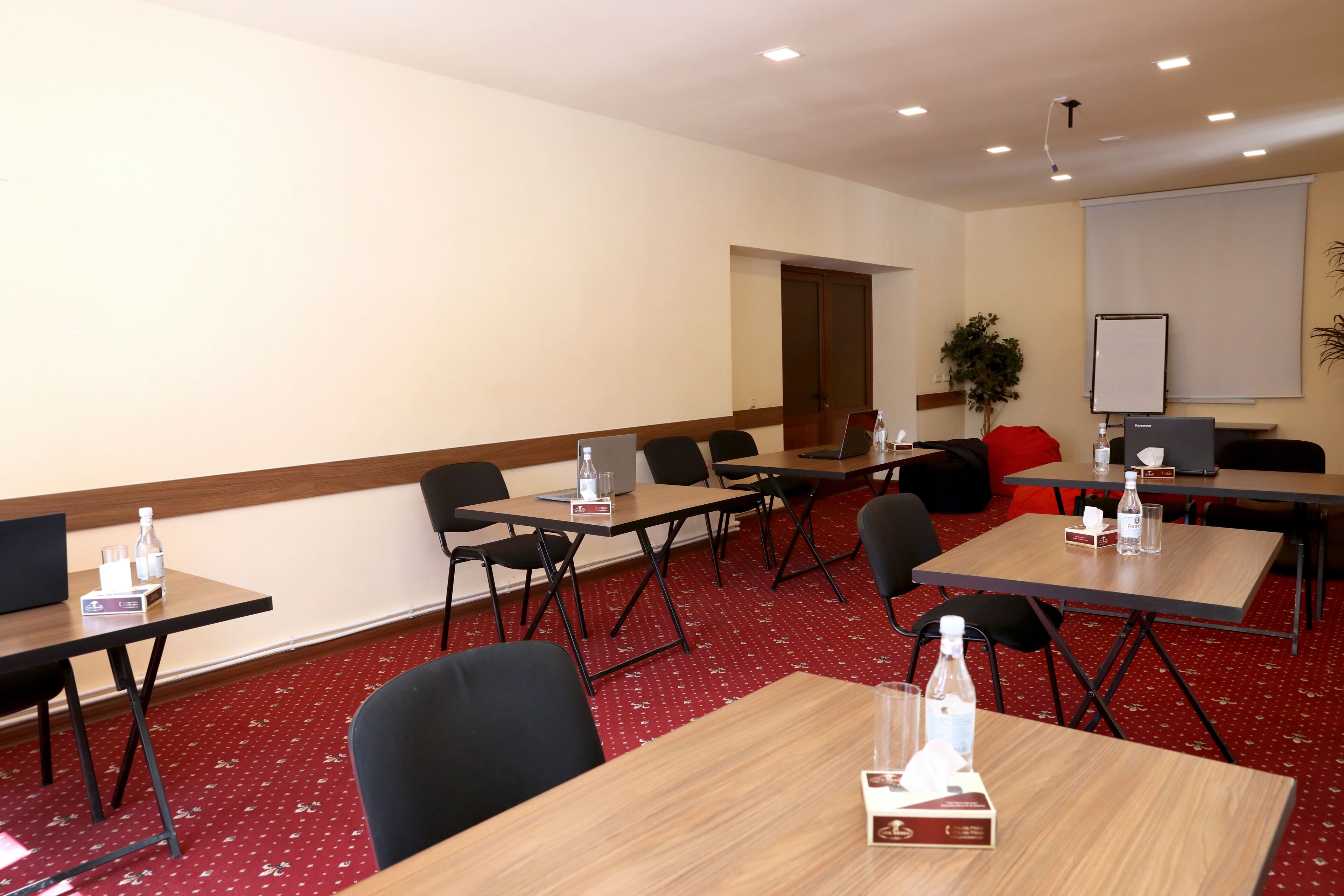 A conference room with tables, chairs, a whiteboard, and a projector screen.