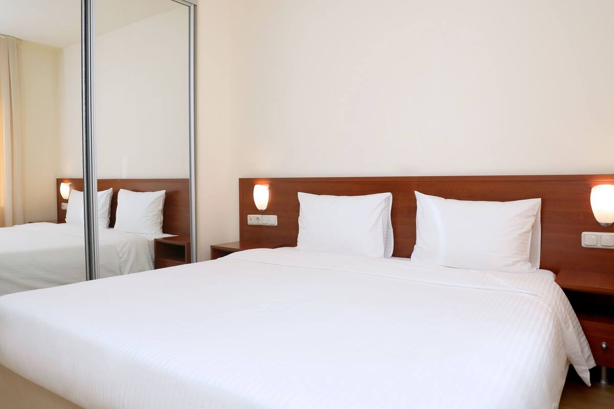 A hotel room with a large bed, a wooden headboard, two bedside tables with lamps, and a full-length mirror.