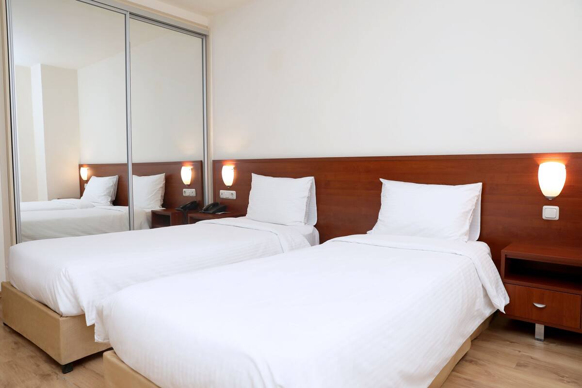 A hotel room with two single beds, a wooden headboard, bedside tables, and a large mirror.