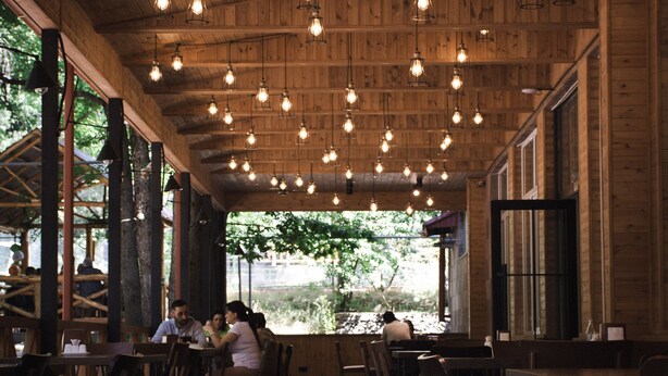 A wooden interior with hanging light fixtures and tables and chairs arranged for dining. - Park Resort Aghveran (Arzakan)