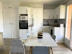 Cozinha compacta com armários brancos, micro-ondas, forno, pia e área de jantar com mesa e cadeiras.