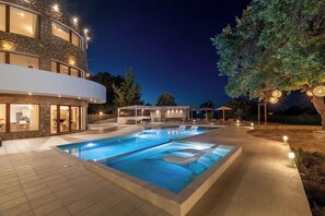 A modern pool area with a stone facade, a covered seating area, and a well-lit outdoor space.