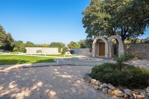 A stone building with a wooden door, surrounded by a gravel driveway and a stone wall.