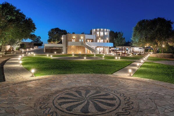 A modern house with a stone facade, a central staircase, and a well-lit outdoor area with a circular mosaic pattern.