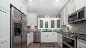 Una cocina moderna con electrodomésticos de acero inoxidable, armarios blancos y un salpicadero de azulejos verdes.