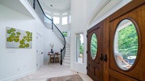 Un vestíbulo amplio con puerta de madera, una escalera y un gran ventanal con vistas a la vegetación.