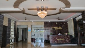 A hotel reception area with a marble reception desk, a chandelier, ceiling fans, and a glass door leading to the interior. - Hotel Clarks Inn Express Bharatpur (Bharatpur)