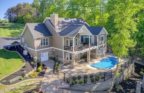 A two-story house with a large front deck, a swimming pool, and a well-maintained lawn.