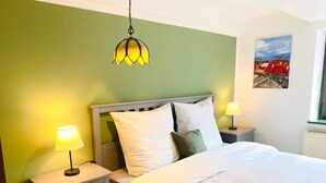 A neatly made bed with white bedding, two bedside lamps, a nightstand with a drawer, and a hanging lamp above the bed. - Cozy apartment at the Engelserker (Pirna)