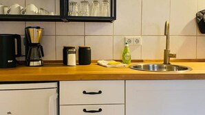 A kitchen with a wooden countertop, a stainless steel sink, and a coffee maker. There are cabinets below the countertop and a refrigerator to the left. - Cozy apartment at the Engelserker (Pirna)