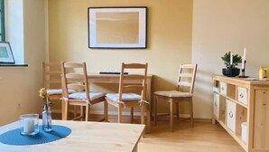 A dining area with a wooden table and chairs, a framed picture on the wall, and a cabinet with drawers. - Cozy apartment at the Engelserker (Pirna)
