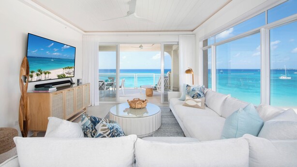 Un salón amplio con un televisor grande, muebles blancos y vista al océano.