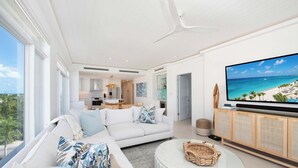 Un salón moderno con un televisor grande, muebles blancos y vista al océano.