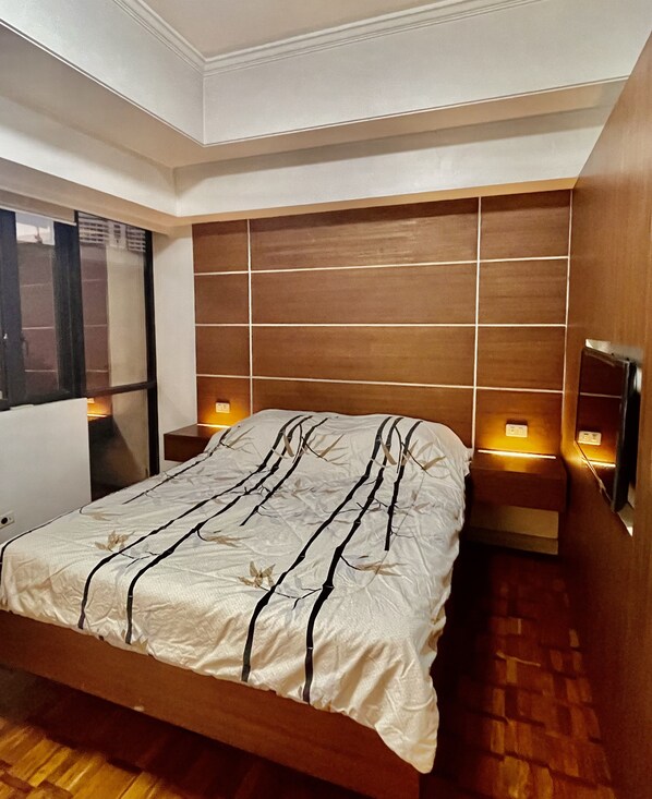 Une chambre à coucher moderne avec une tête de lit en bois, un lit recouvert d’une couvre-lit à rayures noires et blanches, et des lampes de chevet.
