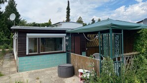 Een klein huis met een groot raam, een overdekte veranda en een grindpad.