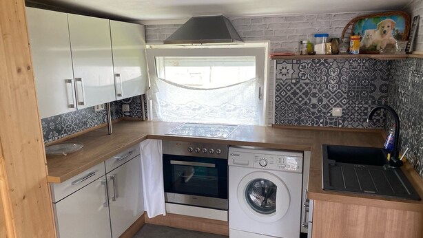 Een compacte keuken met witte kastjes, een inbouwoven, een wasmachine en een spoelbak.