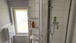 Een compacte badkamer met een raam, een douche en planken met toiletartikelen.