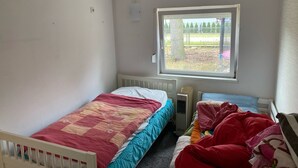 Een slaapkamer met een enkel bed, een radiator en een raam met uitzicht op een omheind buitengebied.