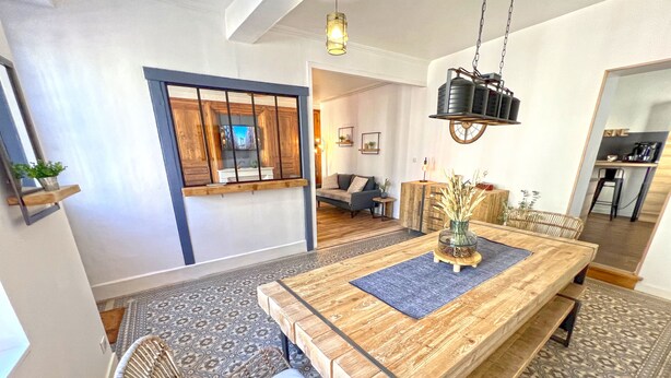 A dining area with a wooden table, benches, and a hanging light fixture. - Stone house with jacuzzi 500m from the Ain 3bed 8p (Poncin)
