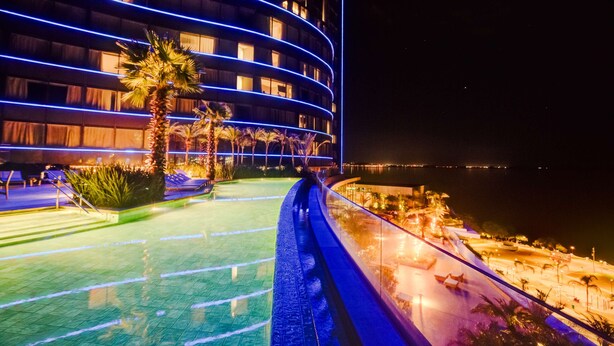 A hotel with a curved facade, outdoor pool, and a view of the sea.