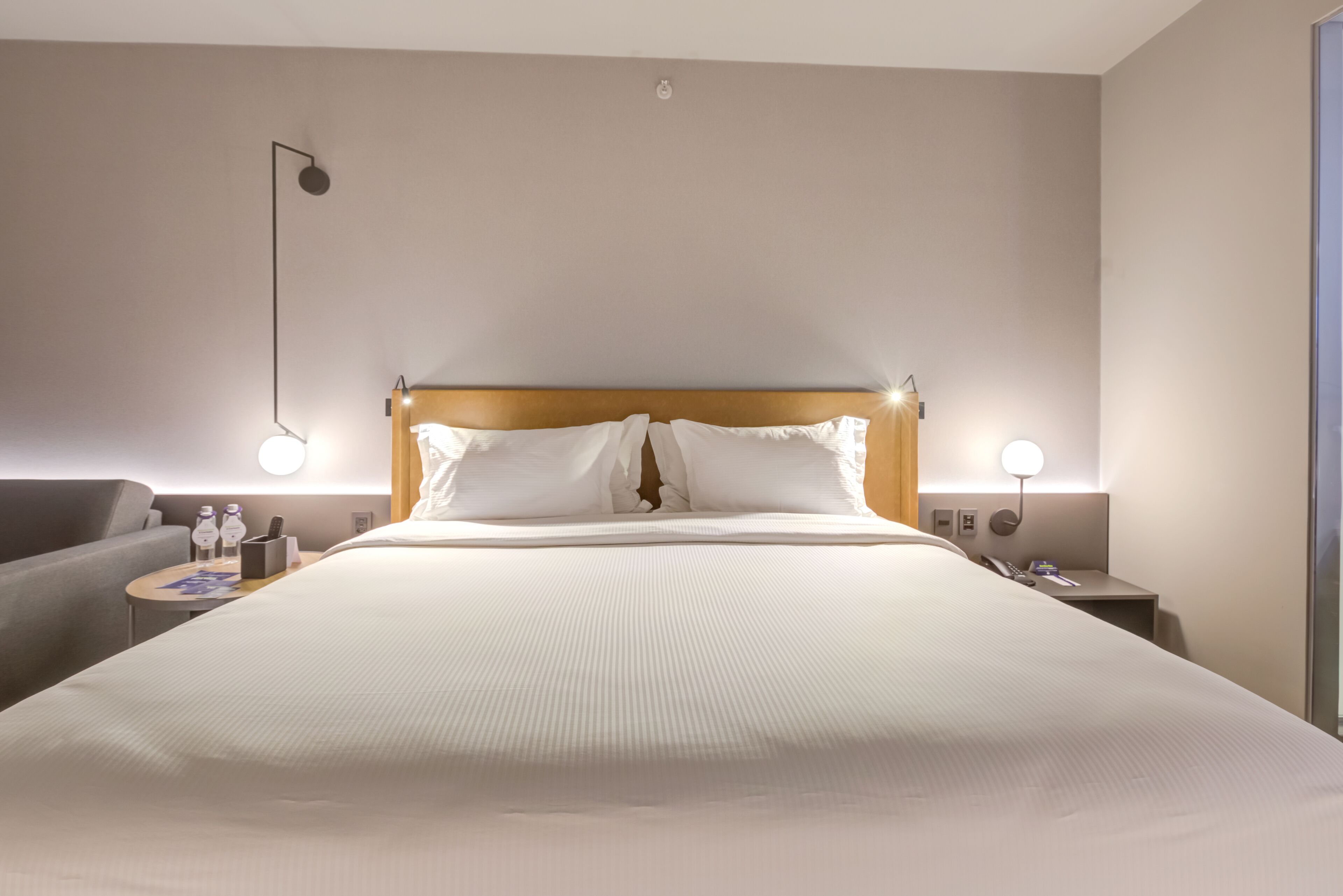 Une chambre d’hôtel avec un grand lit, deux tables de chevet, une petite table, une lampe et un luminaire fixé au mur.