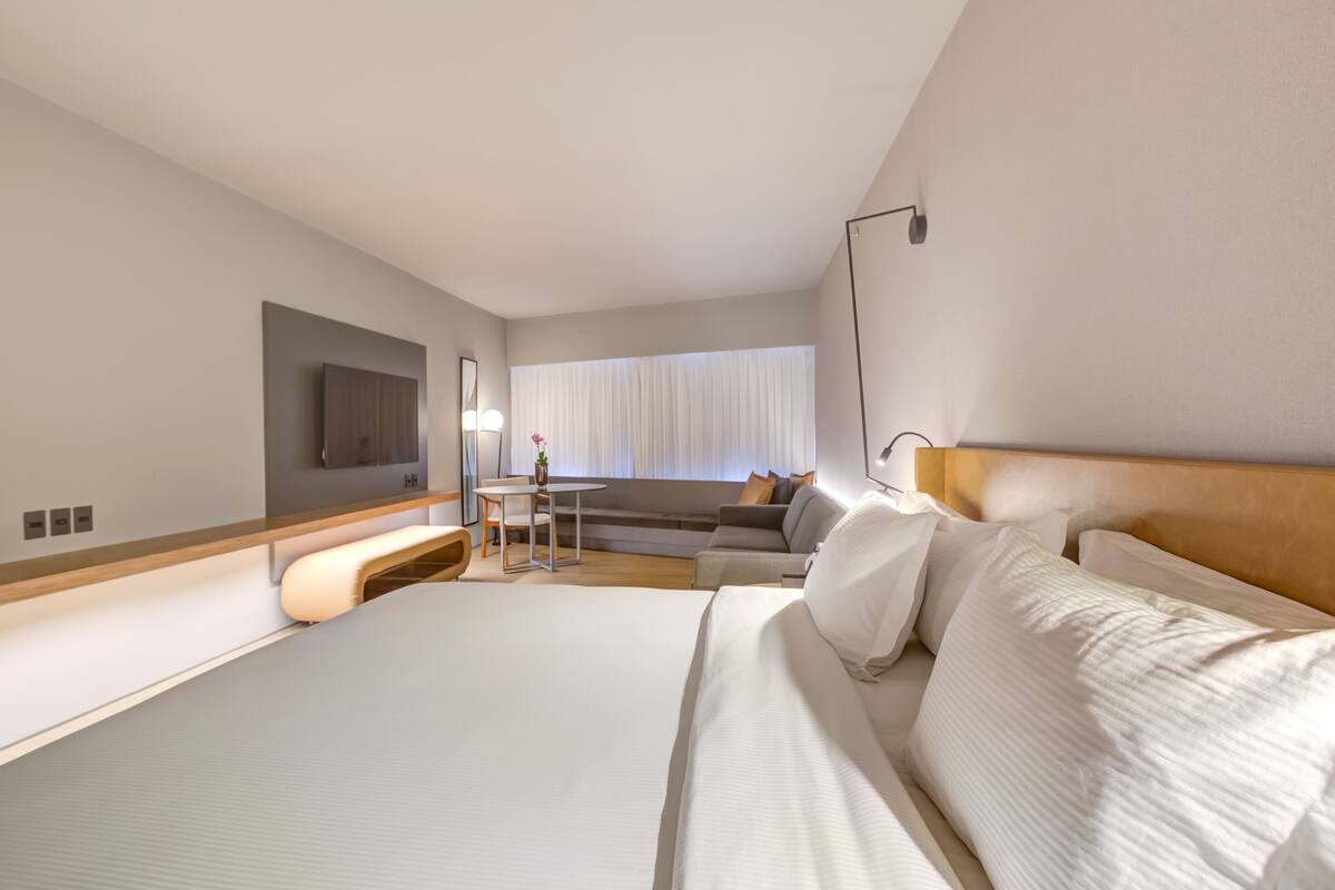 Une chambre d’hôtel moderne, dotée d’un grand lit, d’un canapé, d’une petite table et d’un téléviseur fixé au mur.