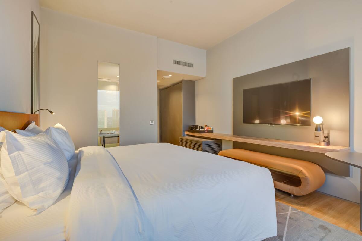 Une chambre d’hôtel moderne avec un grand lit, un banc, une télévision et un miroir.
