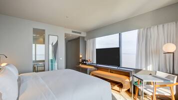 Quarto de hotel moderno com uma cama grande, uma mesa, uma cadeira, uma televisão e vista para o mar.
